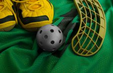 Floorball ball, stick, and shoes on a green jersey.